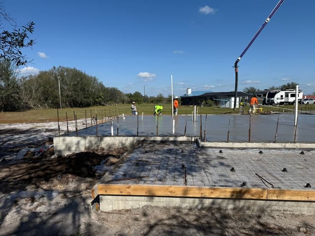 Workers smoothing out a freshly poured concrete slab foundation.